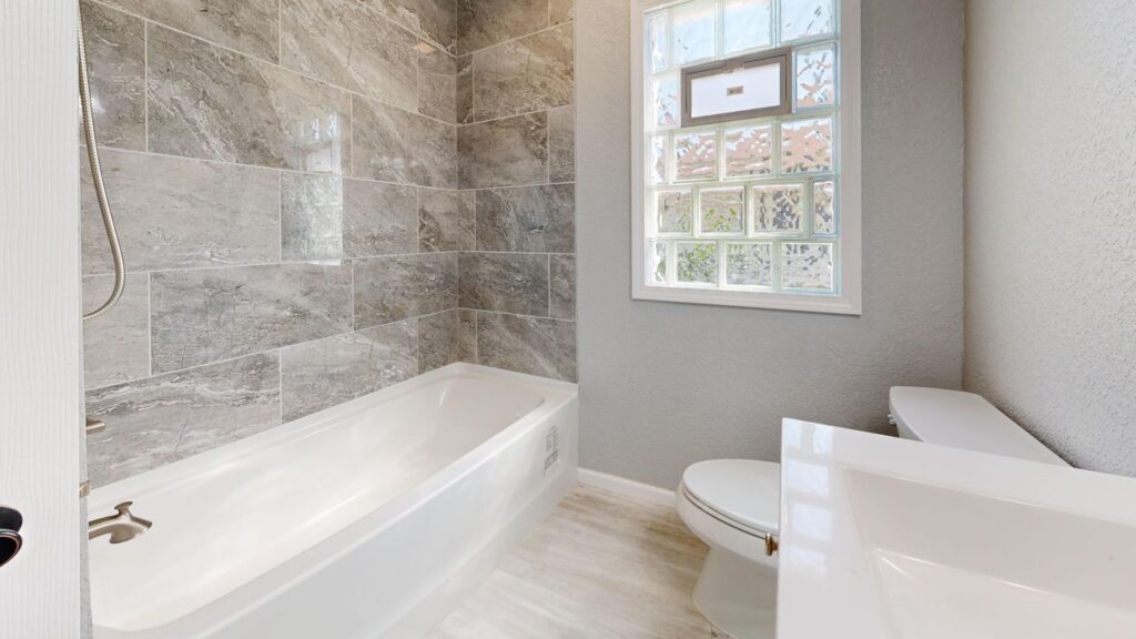Construction Spacious bathroom interior featuring a bathtub, sleek gray tiles, and a glass window.